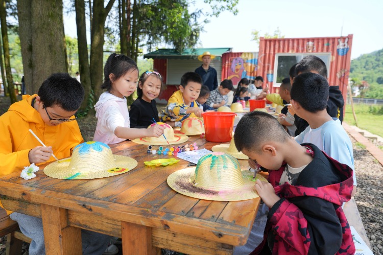 5月5日，北碚區(qū)天府鎮(zhèn)三間田藝術農場，參加研學活動的孩子們在樹林下給草帽繪畫。特約攝影 秦廷富